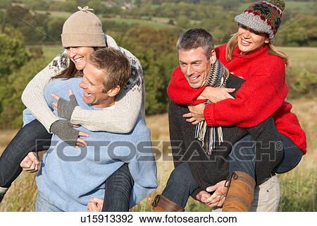 Stock Image - Two Couples Having Piggyback Ride In Autumn Landscape. Fotosearch