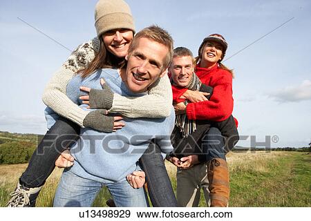 Stock Photo - Two Couples Having Piggyback Ride In Autumn Landscape. Fotosearch