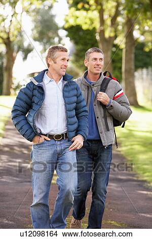 Two Male Friends Walking Outdoors In Autumn Park Together View Large Photo Image Picture - Two Male Friends Walking Outdoors In Autumn Park Together. Fotosearch