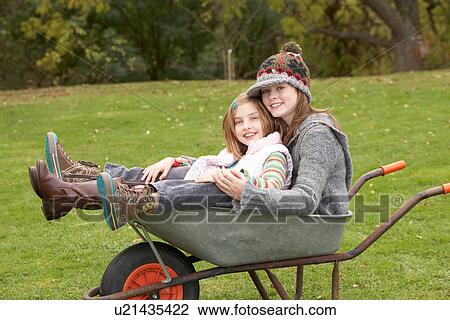 Stock Image - Two Sisters Sitting In Wheelbarrow Outdoors. Fotosearch