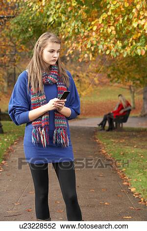 Unhappy Teenage Girl Standing In Autumn Park With Couple On Bench In Background View Large Photo Image Stock Image - Unhappy Teenage Girl Standing In Autumn Park With Couple On Bench In Background. Fotosearch