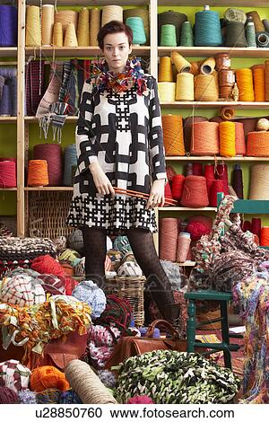 Stock Image - Woman Holding Knitting Needles Standing In Front Of Yarn Display. Fotosearch
