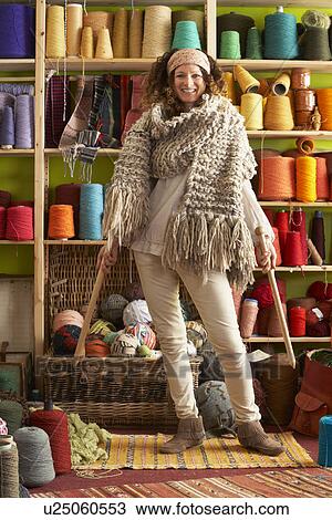 Stock Image - Woman Wearing Knitted Scarf Standing In Front Of Yarn Display. Fotosearch