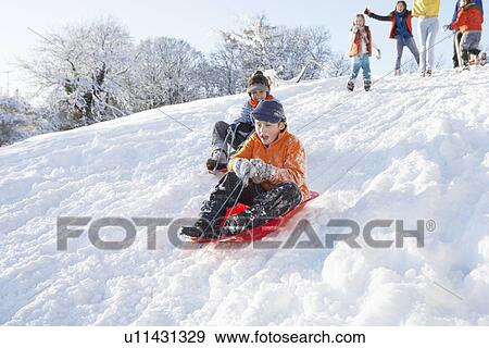 Stock Photo - Young Boy Sledging Down Hill With Family Watching. Fotosearch