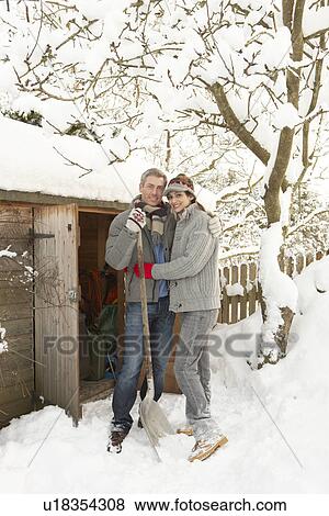 Stock Photo - Young Couple Clearing Snow From Path To Wooden Store. Fotosearch