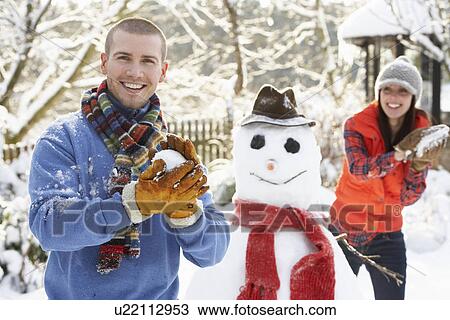 Stock Image - Young Couple Having Snowball Fight In Garden. Fotosearch