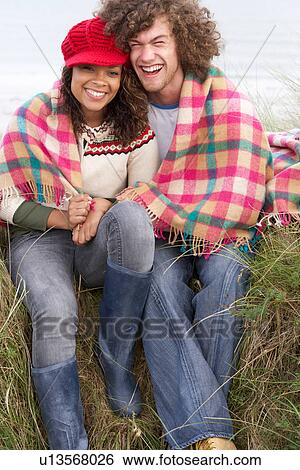 Stock Photograph - Young Couple Sitting In Sand Dunes Wrapped In Blanket. Fotosearch
