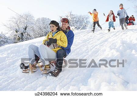 Picture - Young Couple Sledging Down Hill With Family Watching. Fotosearch