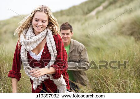 Stock Image - Young Couple Walking Through Sand Dunes Wearing Warm Clothing. Fotosearch