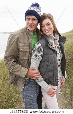 Stock Image - Young Couple Walking Through Sand Dunes Wearing Warm Clothing. Fotosearch