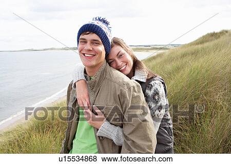 Stock Photo - Young Couple Walking Through Sand Dunes Wearing Warm Clothing. Fotosearch