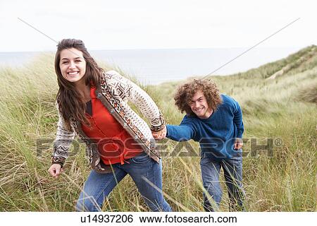 Stock Photograph - Young Couple Walking Through Sand Dunes Wearing Warm Clothing. Fotosearch