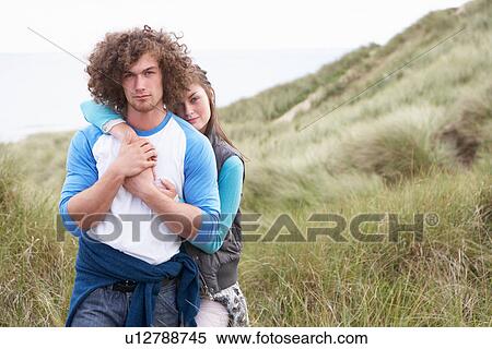 Stock Photography - Young Couple Walking Through Sand Dunes Wearing Warm Clothing. Fotosearch