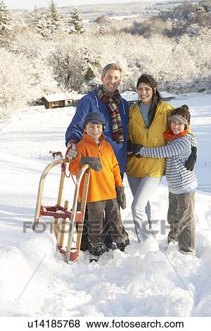 Stock Photo - Young Family Standing In Snowy Landscape Holding Sledge. Fotosearch