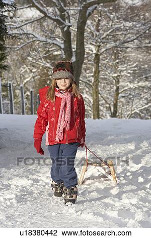 Stock Image - Young Girl Pulling Sledge Through Snowy Landscape. Fotosearch