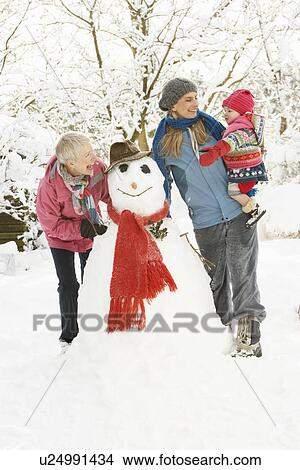 Picture - Young Girl With Grandmother And Mother Building Snowman In Garden. Fotosearch