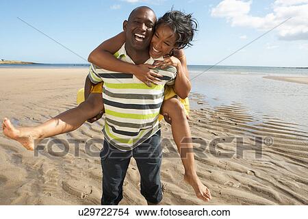 Picture - Young Man Giving Woman Piggyback Along Shoreline Of Beach. Fotosearch