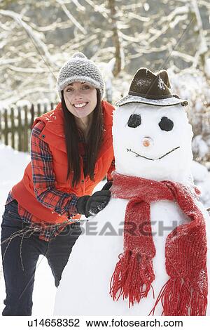 Stock Image - Young Woman Building Snowman In Garden. Fotosearch