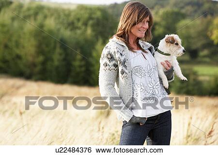 Stock Photograph - Young Woman Outdoors In Autumn Landscape Holding Dog. Fotosearch