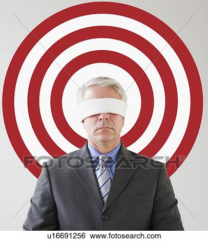 Stock Photograph - Blindfolded man standing in front of bull's eye. Fotosearch