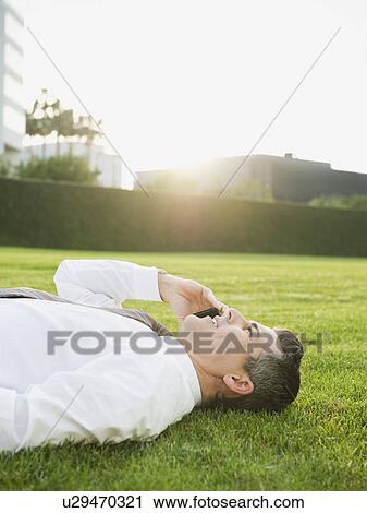 Businessman lying on grass while talking on phone View Large Photo Image Stock Image - Businessman lying on grass while talking on phone. Fotosearch