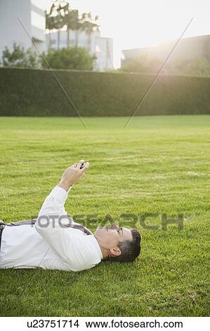 Picture - Businessman texting while lying on grass. Fotosearch