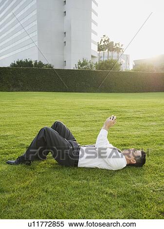 Businessman texting while lying on grass View Large Photo Image Stock Photography - Businessman texting while lying on grass. Fotosearch