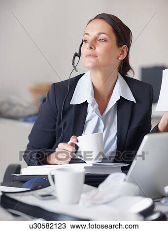 Stock Image - Businesswoman drinking coffee at desk. Fotosearch