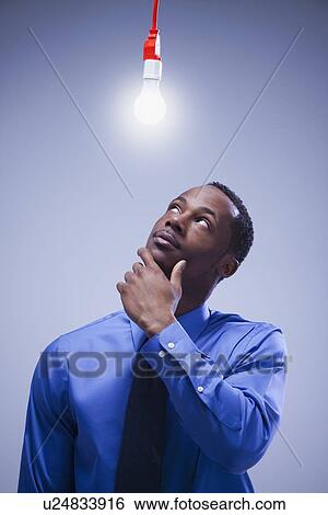 Contemplative businessman standing under a light bulb View Large Photo Image Stock Photograph - Contemplative businessman standing under a light bulb. Fotosearch