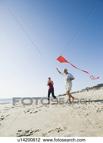 Stock Image - Couple flying kite on beach. Fotosearch