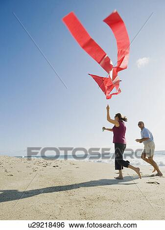 Stock Photograph - Couple flying kite on beach. Fotosearch