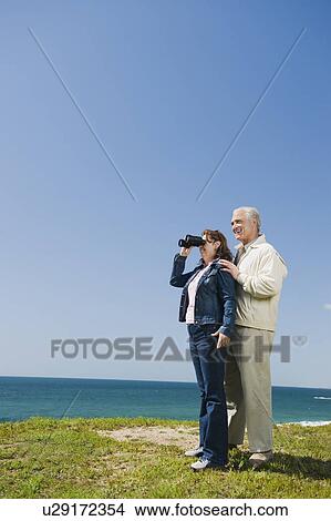 Couple looking at ocean with binoculars View Large Photo Image Picture - Couple looking at ocean with binoculars. Fotosearch