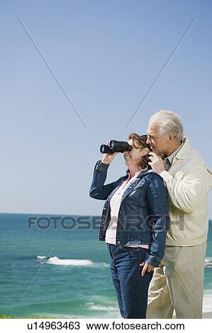 Couple looking at ocean with binoculars View Large Photo Image Stock Image - Couple looking at ocean with binoculars. Fotosearch
