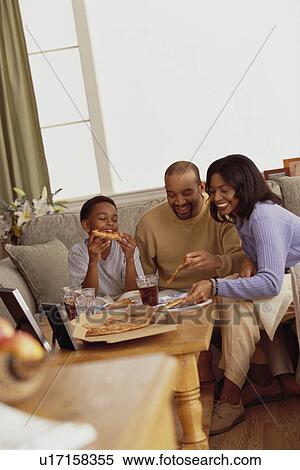 Stock Photography - Family eating pizza in the living room. Fotosearch