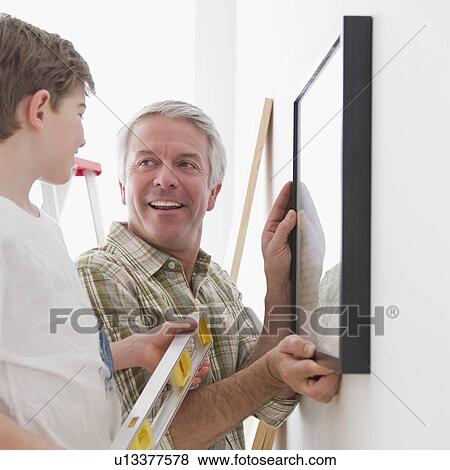 Stock Photo - Father and son hanging picture on wall. Fotosearch