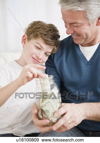 Father and son putting money in jar View Large Photo Image Stock Photo - Father and son putting money in jar. Fotosearch