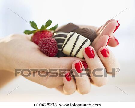 Stock Image - Hand holding chocolates a raspberry and a strawberry. Fotosearch