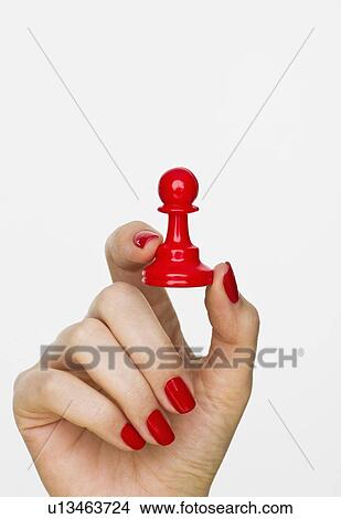 Picture - Hand holding red pawn chess piece. Fotosearch