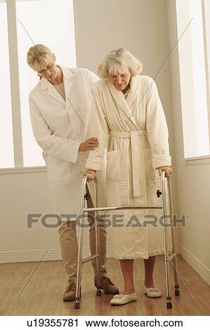 Stock Image - Healthcare worker helping a woman walk with a walker. Fotosearch