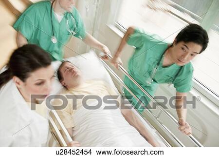 Picture - Healthcare workers pushing gurney in emergency room. Fotosearch