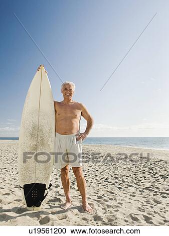 Man holding surfboard on beach View Large Photo Image Stock Image - Man holding surfboard on beach. Fotosearch