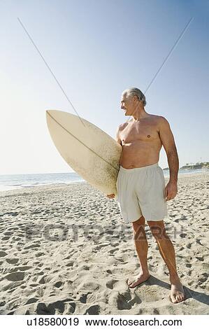 Man holding surfboard on beach View Large Photo Image Stock Photo - Man holding surfboard on beach. Fotosearch
