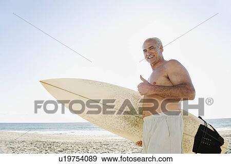 Stock Photo - Man holding surfboard on beach. Fotosearch
