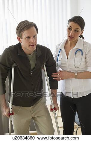 Stock Image - Man walking on crutches in doctor's office. Fotosearch