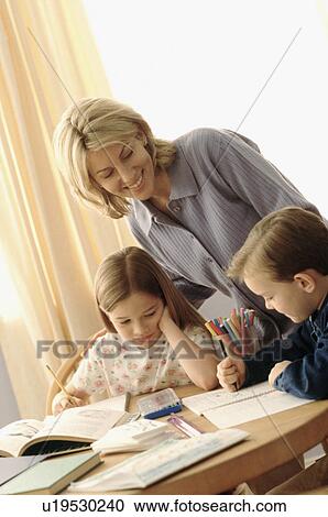 Stock Image - Mother watching her children coloring at the kitchen table. Fotosearch