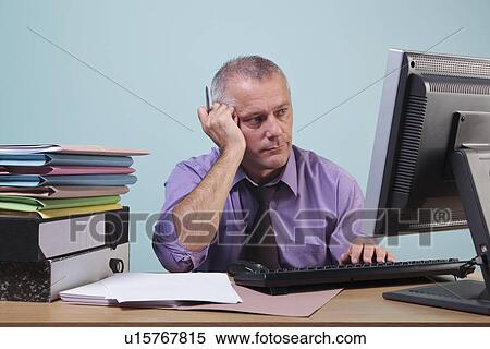 Overworked man sitting at his desk View Large Photo Image Stock Photography - Overworked man sitting at his desk. Fotosearch