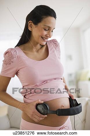 Stock Photograph - Pregnant woman holding headphones on her belly. Fotosearch