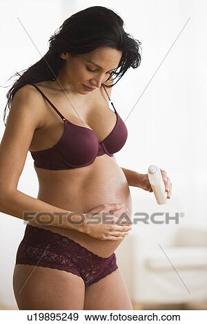 Stock Photo - Pregnant woman putting moisturizing cream on her belly. Fotosearch