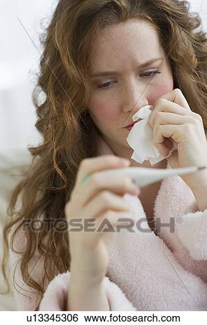 Stock Photograph - Sick woman looking at thermometer. Fotosearch