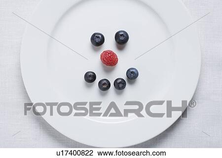 Stock Image - Smiley face of blueberries and raspberry on white plate. Fotosearch